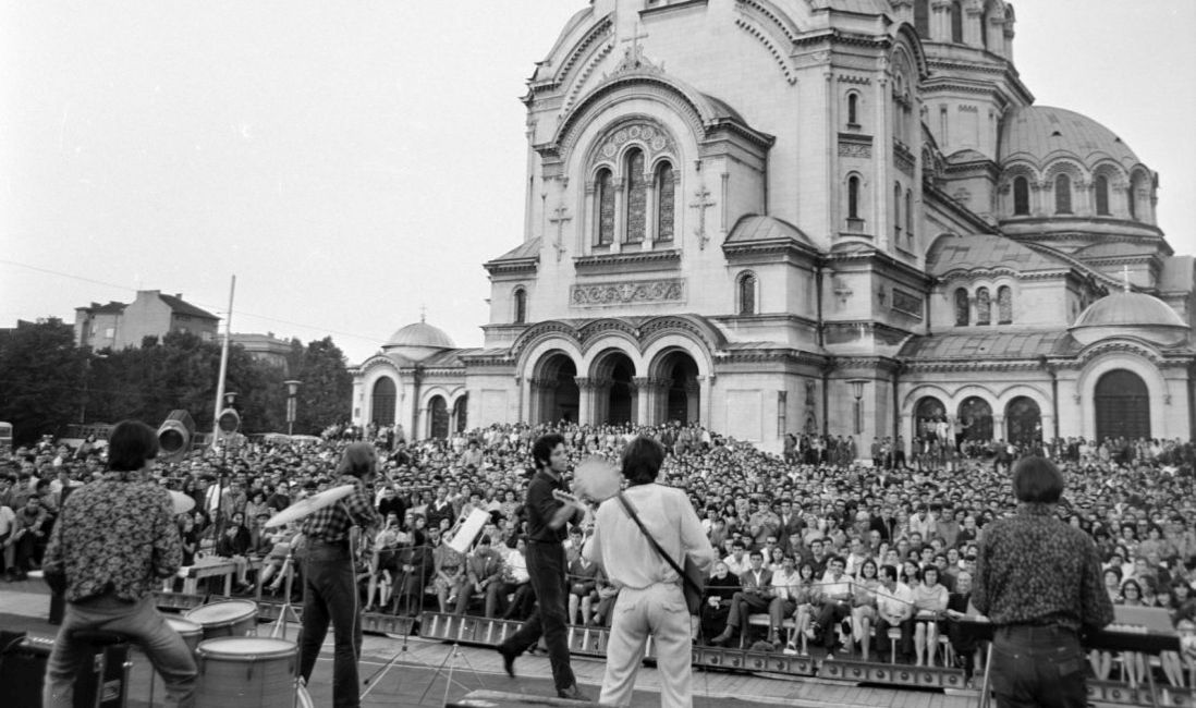 Eine Rockband spielt vor zahlreichem Publikum auf dem Platz vor einer Kirche.